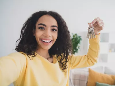 Selfie photo of smiling american happy young girl own her first apartment holding keys relocate to new house indoors loft living room. / Foto: Deagreez