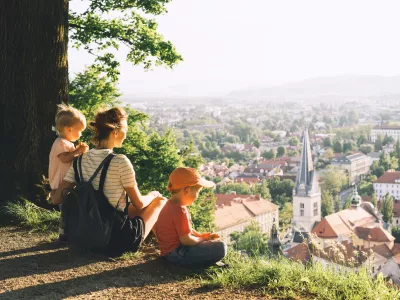 Family on background of Ljubljana, Slovenia, Europe. Woman with two little children looks at panorama of european city from the hill. Mother and kids outdoors at spring or summer time. / Foto: Nataliaderiabina