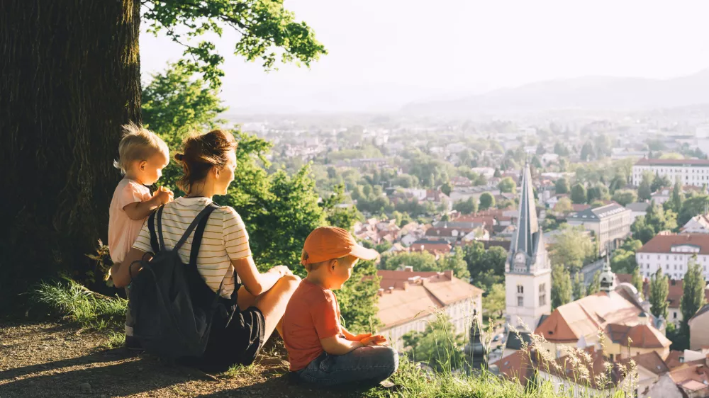 Family on background of Ljubljana, Slovenia, Europe. Woman with two little children looks at panorama of european city from the hill. Mother and kids outdoors at spring or summer time. / Foto: Nataliaderiabina