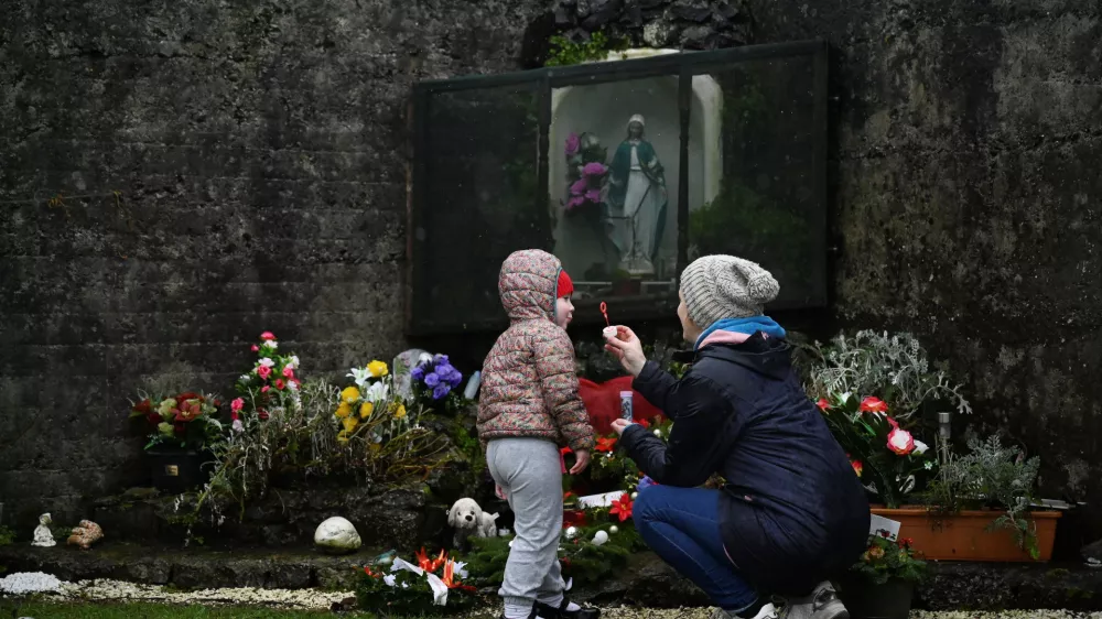 Denise Gormley and her daughter Rosa, 7, pay their respects and blow bubbles at the Tuam graveyard, where the bodies of 796 babies were uncovered at the site of a former Catholic home for unmarried mothers and their children, on the day a government-ordered inquiry into former Church-run homes for unmarried mothers is formally published, in Tuam, Ireland, January 12, 2021. REUTERS/Clodagh Kilcoyne