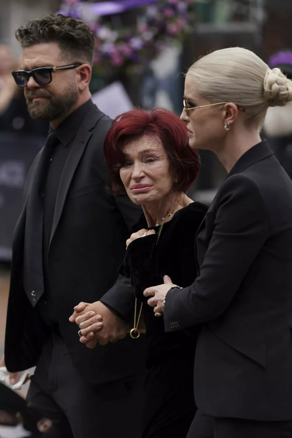 Sharon Osbourne is supported by her children Jack Osbourne and Kelly Osbourne as they arrive to lay and view the flowers left at the Black Sabbath Bridge bench on Broad Street in memory of Black Sabbath frontman Ozzy Osbourne during his funeral procession, in Birmingham, England, Wednesday July 30, 2025. (Joe Giddens/PA via AP)