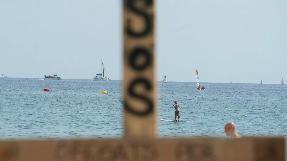 People are seen sailing behind a wooden cross placed by lifeguards, which has the word "drowned" written on it, as lifeguards protest on the shortage of personnel and precarious instalments along the beaches, following more than 700 drownings last year across Spain, according to the Royal Spanish Lifeguard and First Aid Federation, in Barcelona, Spain August 1, 2025. REUTERS/Bruna Casas