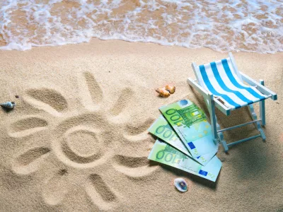 Deckchair with euro bills on a beach with a sun drawn on the sand. Travel money savings concept