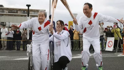 Torchbearer Shigeko Kagawa, left, hands over the flame of the torch to the next runner during a torch relay event for the Tokyo Olympics in Yamatokooriyama, Nara prefecture, western Japan, April 12, 2021. (Kyodo News via AP)