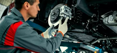 Car mechanic worker repairing suspension of lifted automobile at auto repair garage shop station
