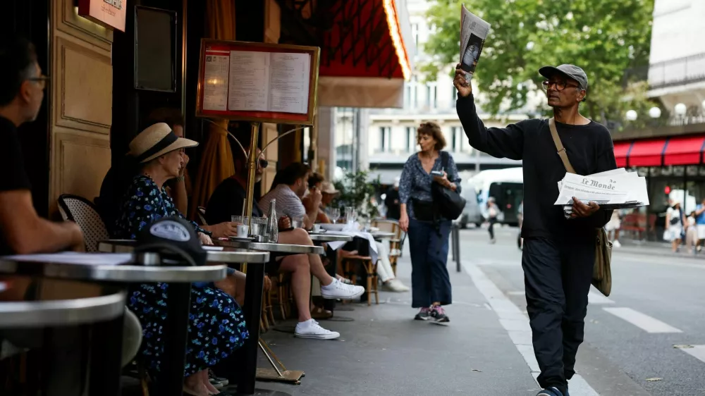 Ali Akbar, 73, known as the last newspaper hawker in the French capital sells 'Le Monde' newspaper to people on a terrace in the Latin Quarter, in Paris, France, August 4, 2025. REUTERS/Stephanie Lecocq / Foto: Stephanie Lecocq