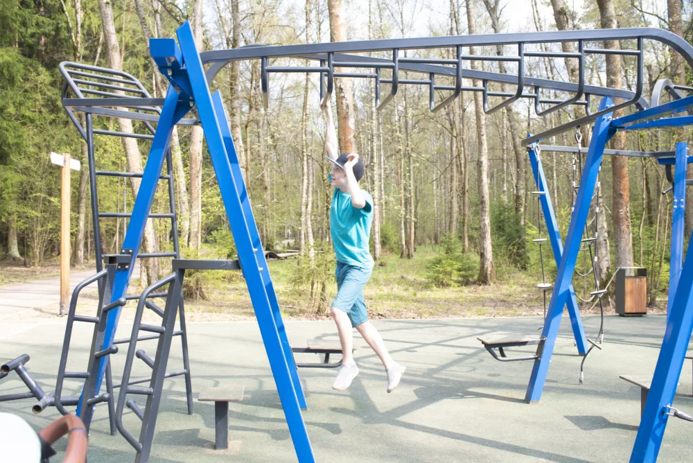 boy hanging by his hands and moving along a horizontal ladder (monkey walker) on a sports ground