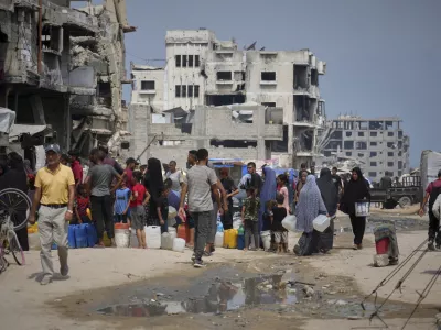 In the summer heat, Palestinians line up to collect water from a distribution point in Gaza City, Tuesday, Aug. 12, 2025. (AP Photo/Jehad Alshrafi)