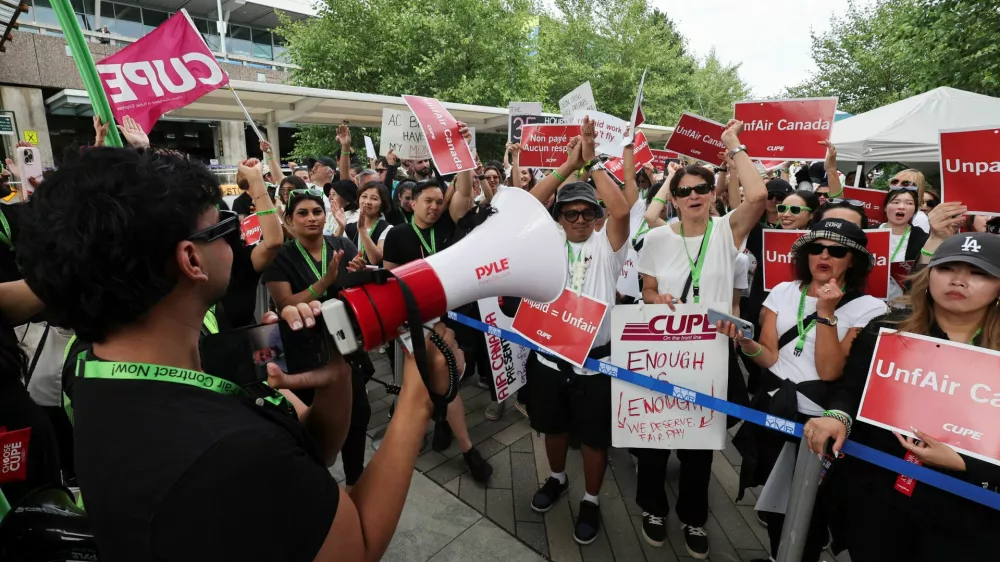 CUPE president Mark Hancock appears on a mobile phone screen as striking Air Canada flight attendants listen to a remote broadcast by megaphone by Hancock on the current situation, as they defy a back to work order at Vancouver International Airport in Richmond, British Columbia, Canada August 18, 2025. REUTERS/Chris Helgren