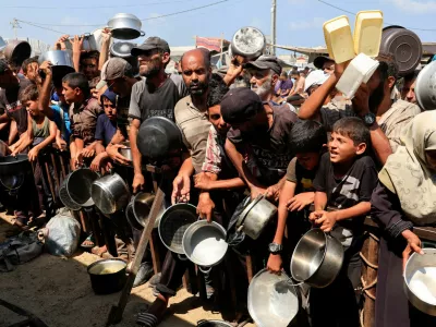 FILE PHOTO: Palestinians hold pots and containers while waiting to receive food from a charity kitchen in Khan Younis, southern Gaza Strip, August 21, 2025. REUTERS/Hatem Khaled/File Photo