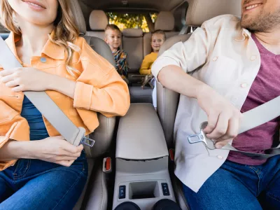 Smiling parents holding safety belts near kids on blurred background in car / Foto: Lightfieldstudios