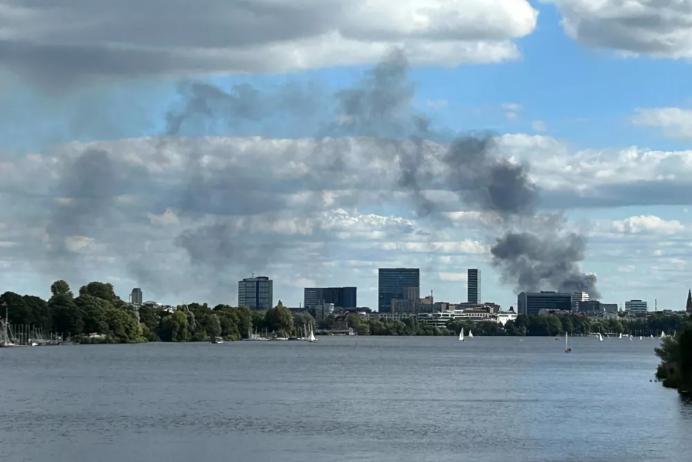 25 August 2025, Hamburg: A large cloud of smoke can be seen over the city of Hamburg, from the Krugkoppel Bridge at the end of the Outer Alster. A fire has broken out in a warehouse in the Port of Hamburg, causing a major motorway nearby to be closed. Photo: Michael Rummler/dpa