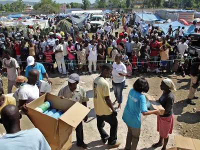 HAITI - On 24 January, Haitian aid workers and UNICEF and World Food Programme staff prepare to distribute relief supplies in the Pinchinat camp for people displaced by the earthquake, on a football pitch in the city of Jacmel. Supplies include bedding, water jugs, kitchen items and mosquito bed nets. Several UNICEF staff members wear T-shirts bearing the UNICEF logo. In a joint rapid response, UNICEF and the World Food Programme (WFP) are providing a daily hot meal for the estimated 5,000 people living in the camp. Assisted by MINUSTAH, the two agencies are also providing safe water in the camp. Some 34,000 people in Jacmel have been affected by the quake.On 24 January 2010 in Haiti, humanitarian assistance for survivors of the 7.3 magnitude earthquake that hit the country on 12 January continues to improve as capacity and logistical constraints are addressed. The quakes epicentre was only 17 kilometres from Port-au-Prince, the capital, and needs remain great. Quake aftershocks on 20 and 23 January caused further damage, especially in the town of Petit Goave. Unaccompanied children who have lost or been separated from their families are among the most vulnerable. Revised estimates by the Government report that more than 112,000 people were killed during the quake and 1.5 million have been left homeless. In Port-au-Prince, estimated numbers of people living in makeshift shelters range from 370,000800,000, despite the recent exodus of as many as 235,000 from the devastated city. Major government and private infrastructure have been destroyed or heavily damaged, including hospitals, water, sanitation and electrical systems, and telecommunications, banks and transportation networks. United Nations and UNICEF buildings and residences were also hit, and UN staff and peacekeepers with the UN Stabilization Mission in Haiti (MINUSTAH) are missing and more than 50 are confirmed to have died. MINUSTAH, totalling 7,000 peacekeepers and 2,000 police, have relocated their logistics base close to the airport to better coordinate incoming international relief assistance. The UN Consolidated Flash Appeal for the Haiti earthquake emergency requests US 5 million for relief and recovery for the next six months. UNICEFs portion of the appeal is US 7.9 million and UNICEF is the lead coordinating agency for education, child protection, nutrition and WASH (water, sanitation and hygiene). Working with the Government, other UN agencies, international and local NGOs and private partners, UNICEF is distributing safe water and equipment and health and shelter supplies, and establishing child feeding centres for children under age five. UNICEF is also working with partners to establish safe spaces for unaccompanied children and implementing procedures to identify, register and help reunite them with their families. Support has also been given to the Government to monitor children who are departing the country, to ensure that proper documentation and permissions are in place. This latest catastrophe exacerbates Haitis already critical humanitarian situation. An estimated 46 per cent of its nearly 10 million inhabitants are under age 18, and more than 78 per cent of the population lives on less than US .00 a day.