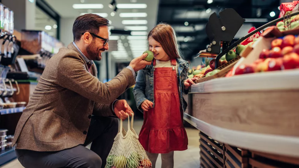 Father and daughter smiling apple, tasting quality while buying groceries in market