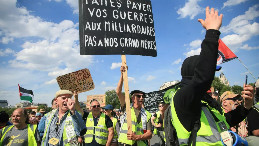 Demonstranti med leto&scaron;njimi delavskim praznikom. Na transparentu pi&scaron;e: Za va&scaron;e vojne naj plačajo milijarderji, ne na&scaron;e babice.