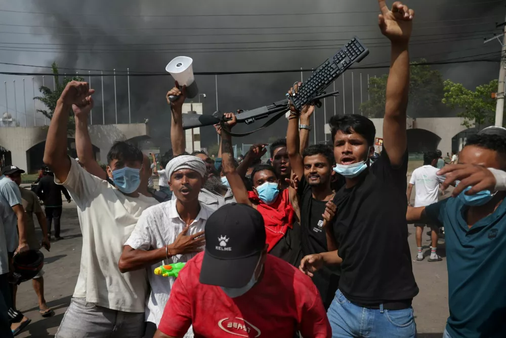 Demonstrators react as smoke rises from the Parliament complex following fire set up by protesters during a protest against Monday's killing of 19 people after anti-corruption protests that were triggered by a social media ban, which was later lifted, during a curfew in Kathmandu, Nepal, September 9, 2025. REUTERS/Adnan Abidi