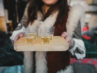 Shallow depth of field (selective focus) image with a woman holding a wooden plate with palinca (or tuica), romanian traditional plum brandy.