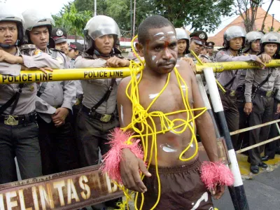 A Papuan protester stands near riot police officers during a demonstration in Surabaya, East Java, Indonesia, Wednesday, March 22, 2006, demanding that U.S. mining giant Freeport close its massive gold mine in Papua province. Indonesia is sending hundreds more police troops to the province to prevent further unrest as the number of security officers killed in protests there last week rose to five. (AP Photo/Trisnadi)