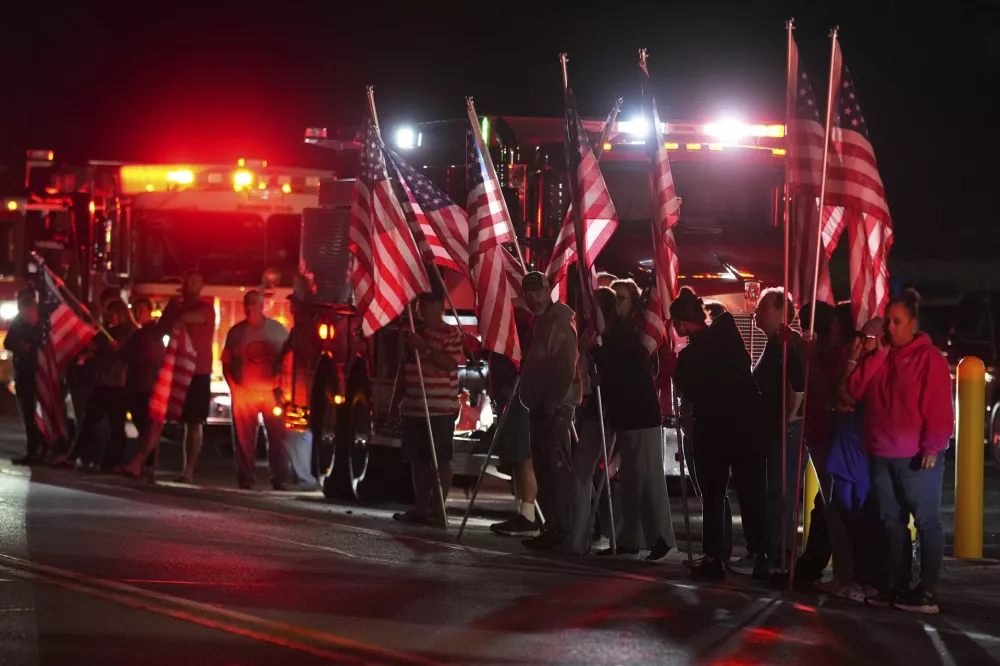 People hold American flags before a procession Wednesday, Sept. 17, 2025, in Spring Grove, Pa., after multiple police officers were shot and killed. (AP Photo/Matt Slocum)