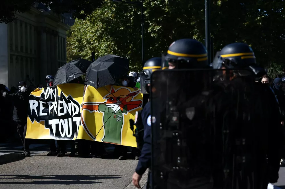 French CRS riot police stand on position as masked protesters holding umbrellas and a banner attend a demonstration in Nantes as part of a day of nationwide strikes and protests against the government and cuts in the next budget, with supporters of the "Bloquons Tout" (Let's Block Everything) movement, France, September 18, 2025. The slogan reads "We take everything back". REUTERS/Stephane Mahe