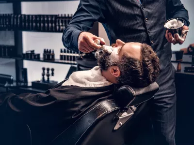 Barber applies shaving foam to a man's face in a saloon. / Foto: Fxquadro