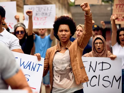 Multi-ethnic crowd of people protesting against racism on city streets. Focus is on African American woman with raised fist. / Foto: Drazen Zigic