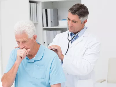Male doctor examining coughing senior patient in clinic