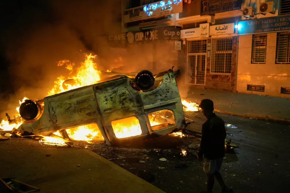 A boy stands next to a torched police vehicle as youth led protests calling for healthcare and education reforms turned violent, in Sale, Morocco, Wednesday, Oct. 1, 2025. (AP Photo/Mosa'ab Elshamy)