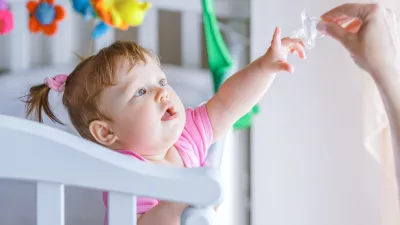 Little girl pulls her hand to the dummy, standing in a baby crib