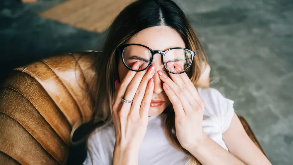 Young woman rubs her eyes after using glasses. Eye pain or fatigue concept. / Foto: Nikkimeel