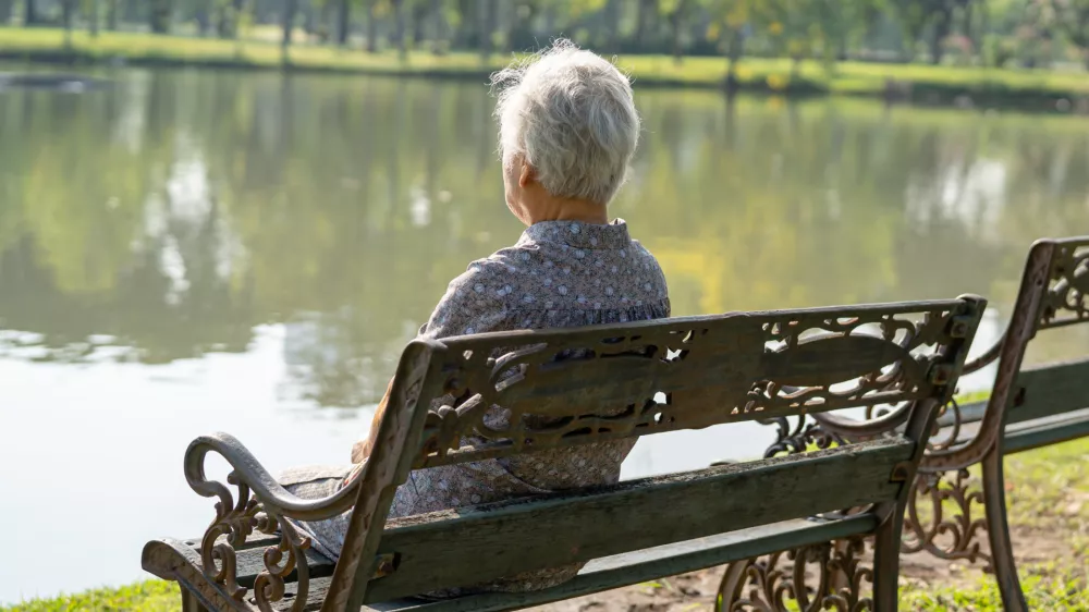 Asian elderly woman depressed and sad sitting back on bench in autumn park.