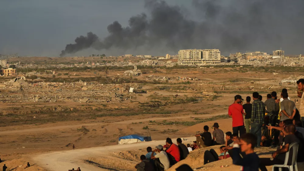 Displaced Palestinians watch smoke rise after Israeli military strikes as they gather on the coastal road near Wadi Gaza, in the central Gaza Strip, Thursday, Oct. 9, 2025. (AP Photo/Abdel Kareem Hana)