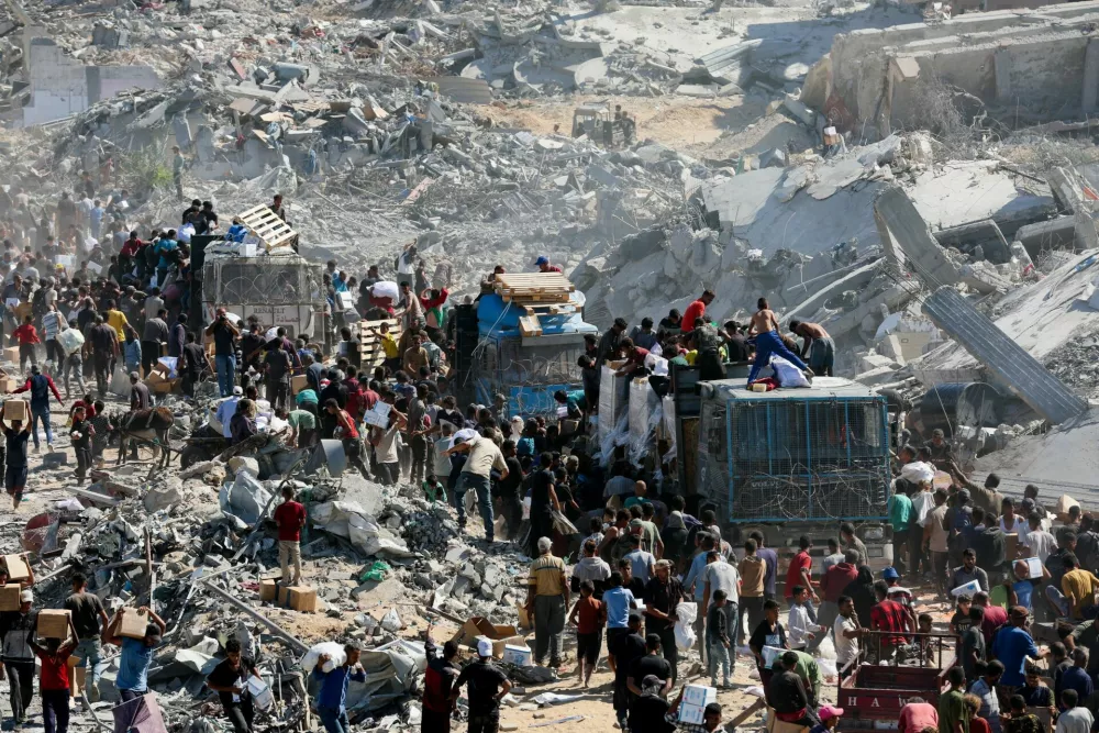 Palestinians collect aid supplies from trucks that entered Gaza, amid a ceasefire between Israel and Hamas, in Khan Younis, in the southern Gaza Strip October 12, 2025. REUTERS/Ramadan Abed