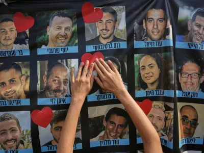 A person pastes a heart-shaped sticker on a banner with pictures of Israeli hostages during a a gathering at a plaza known as hostages square in Tel Aviv, Israel, Monday, Oct. 13, 2025. (AP Photo/Oded Balilty)