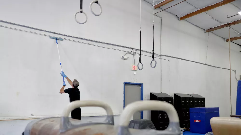 Southwest Gymnastics Training Center owner Brock Anstine cleans walls in his gym Monday, March 23, 2020, in Tempe, Ariz. Anstine, in compliance with CDC guidelines to help slow the spread of the COVID-19 coronavirus, has closed his gym and is paying his staff to deep cleans and paint the facility during their shut down. (AP Photo/Matt York)