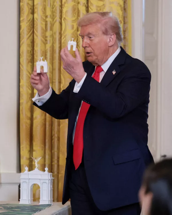 U.S. President Donald Trump holds models of an arch monument during a ballroom dinner in the East Room at the White House in Washington, D.C., U.S., October 15, 2025. REUTERS/Jonathan Ernst