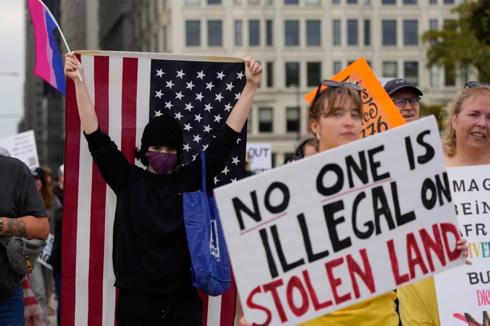 People hold signs and an American flag before a "No Kings" protest Saturday, Oct. 18, 2025, in Chicago. (AP Photo/Nam Y. Huh)