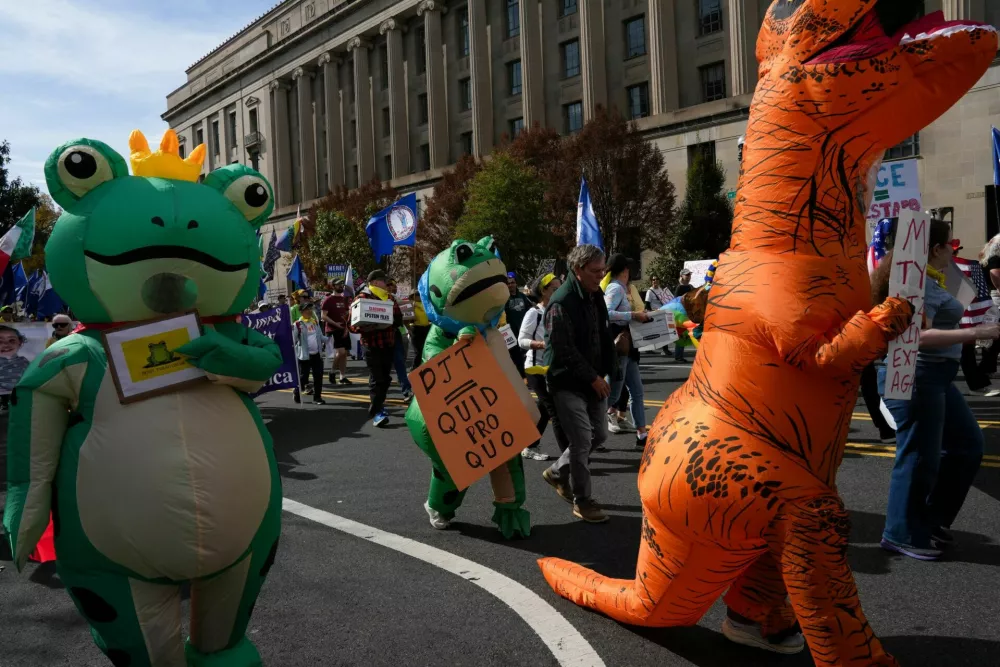 Demonstrators wearing frog costumes walk behind a protester wearing a T-Rex costume during a "No Kings" protest against U.S. President Donald Trump's policies, in Washington, D.C., U.S., October 18, 2025. REUTERS/Leah Millis