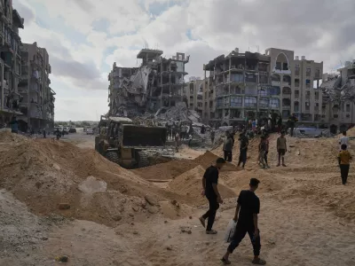 Palestinians watch members of the Hamas militant group searching for bodies of the hostages in an area in Hamad City, Khan Younis, in the southern Gaza Strip, Saturday, Oct. 18, 2025. (AP Photo/Jehad Alshrafi)