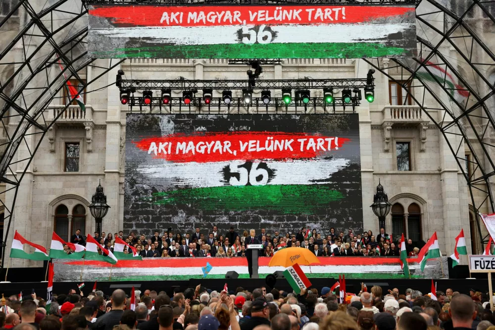 A text reading "Those who are Hungarian are coming with us" is displayed in the background as Hungarian Prime Minister Viktor Orban delivers a speech to mark the 69th anniversary of the Hungarian Uprising of 1956, in Budapest, Hungary, October 23, 2025. REUTERS/Bernadett Szabo