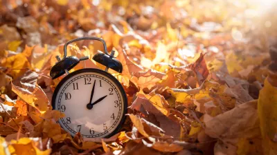 Alarm clock among golden yellow fall leaves with bright sunshine, autumn time change concept / Foto: Juliealexk