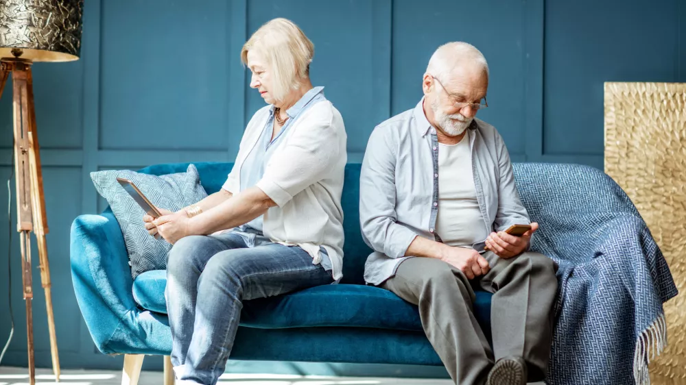 Offended senior man and woman sitting back to each other, using digital gadgets on the couch at home / Foto: Rosshelen