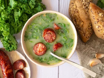 Portuguese style soup called Caldo Verde, bread, Cabbage julienne, and chorizo sausage on a white wooden Table. Flat lay / Foto: Iggi_boo