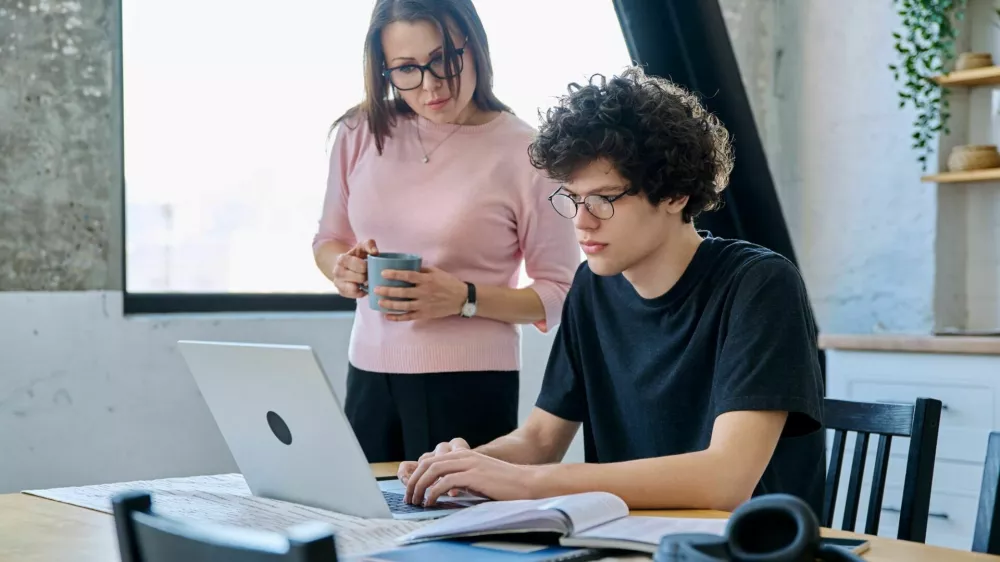 Middle aged mother and son university student, together at home in the kitchen, serious guy and woman talking looking at computer laptop. Communication, relationship, lifestyle, family concept / Foto: Valeriy_g