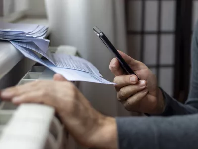 Freezing man holding phone and check bills for electricity, gas and heating. Increase in the cost of gas bill. Soaring energy prices. Increase in the price of natural gas. Energy crisis in Europe. / Foto: Anastasija Vujic, Istock