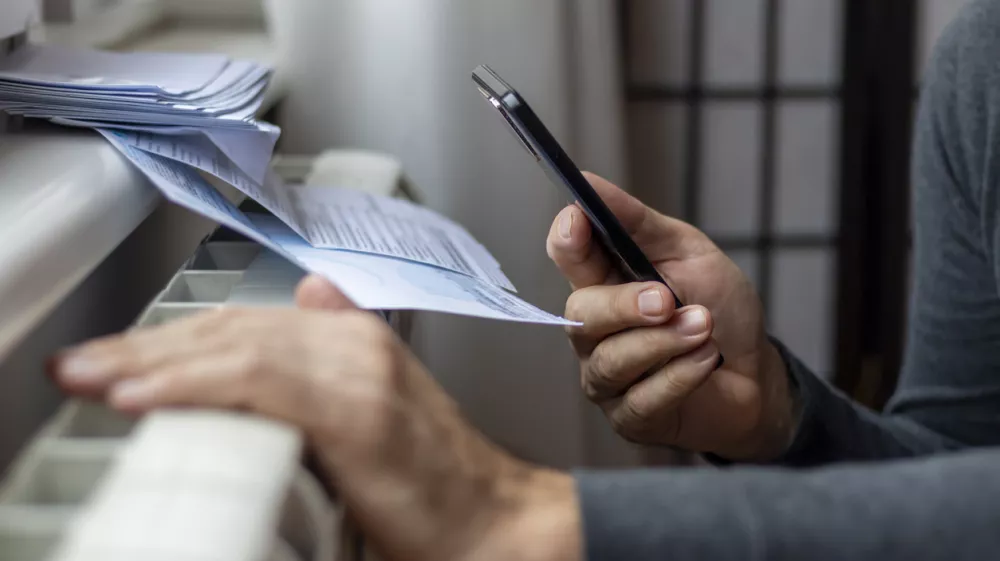 Freezing man holding phone and check bills for electricity, gas and heating. Increase in the cost of gas bill. Soaring energy prices. Increase in the price of natural gas. Energy crisis in Europe. / Foto: Anastasija Vujic, Istock