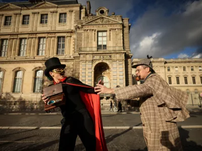 Members of the Paris Holmes Society (Cercle Holmesien de Paris), Laurence Deloision, dressed like Arsene Lupin, left, and Thierry Gilibert, dressed like Sherlok Holmes, stage the theft by the facade and the window where thieves entered the Louvre museum last Sunday, Saturday, Oct. 25, 2025 in Paris. (AP Photo/Thomas Padilla)