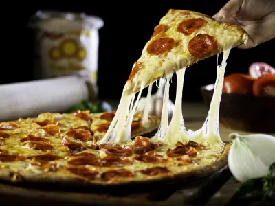 A person getting a piece of cheesy pepperoni pizza / Foto: Wirestock