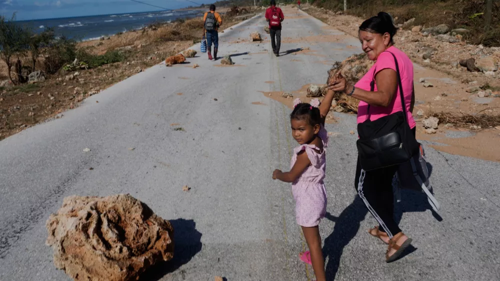 People pass by rocks washed onto a road by Hurricane Melissa on the southern coast of Santiago de Cuba, Thursday, Oct. 30, 2025. (AP Photo/Ramon Espinosa)
