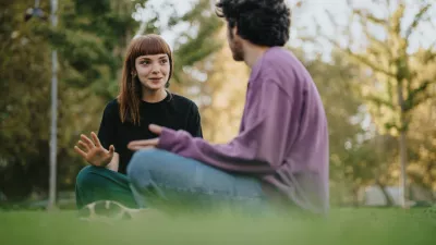 Two young people engage in a friendly conversation while sitting on the grass outdoors. The scene reflects friendship, connection, and relaxation in a green, sunlit environment. / Foto: Qunicastudio